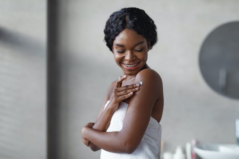 Sensual african american young woman using skin softener, bathroom interior